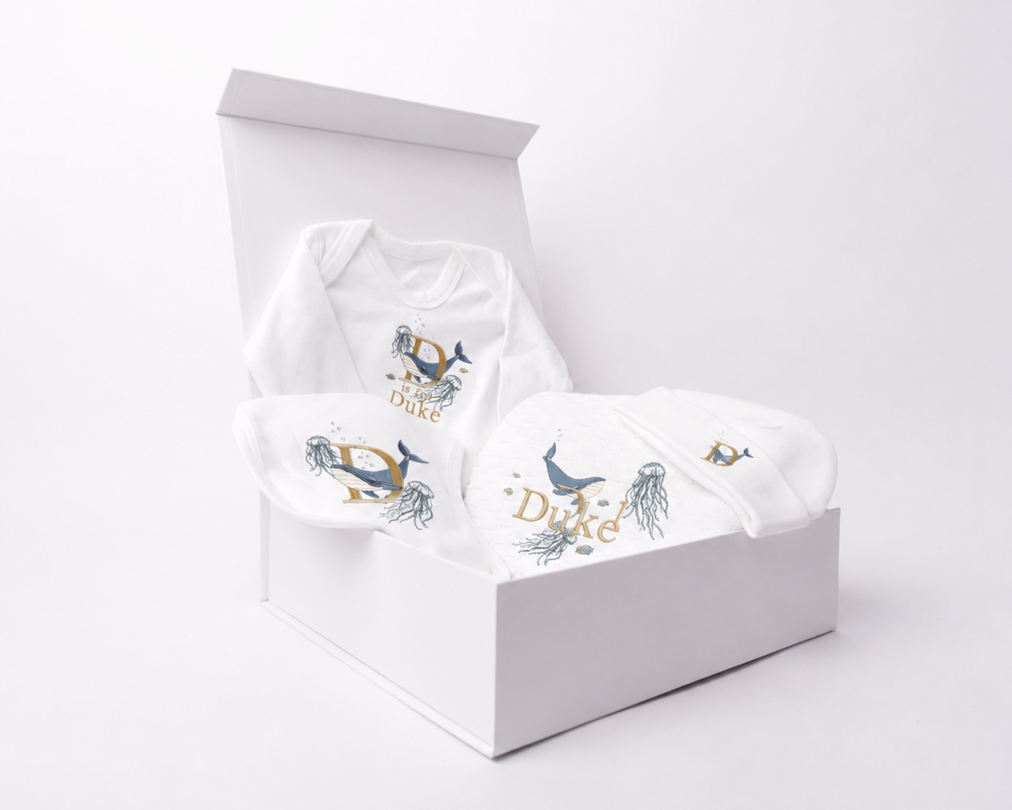 Underwater World embroidered gift set displayed inside an open white gift box on a clean white background. Featuring embroidery bib, romper, blanket and beanie, personalised with the name Duke