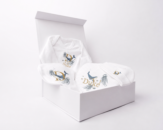 Underwater World embroidered gift set displayed inside an open white gift box on a clean white background. Featuring embroidery bib, romper, blanket and beanie, personalised with the name Duke
